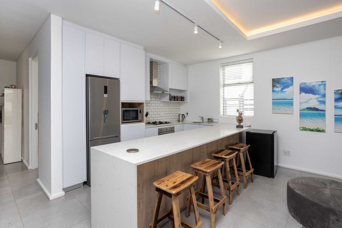 Modern kitchen featuring white cabinetry, quartz countertops, subway tile backsplash, integrated appliances, and a breakfast bar with recessed and cove lighting.