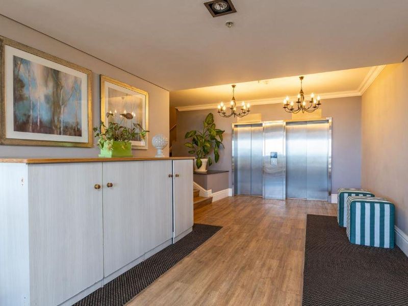 A well-maintained apartment building lobby featuring stainless steel elevator access, wood-look flooring, and built-in storage cabinetry.