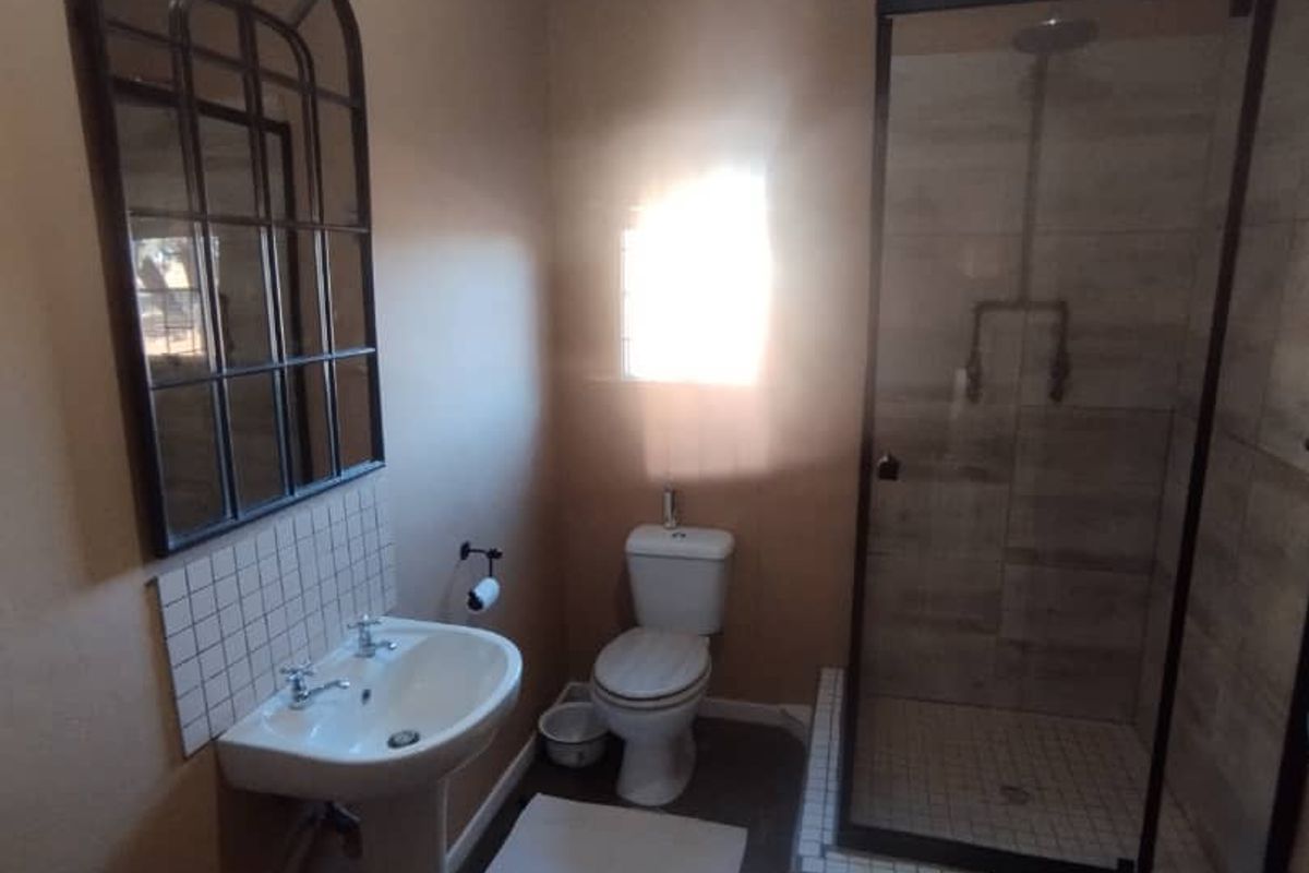 A functional bathroom featuring a pedestal basin, a toilet, and a glass-enclosed shower with tiled surround.