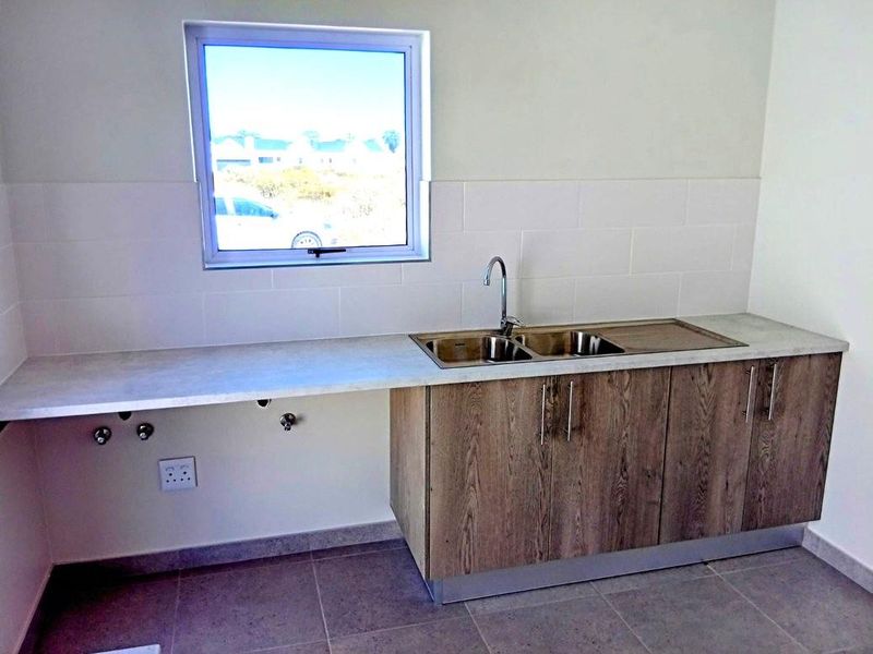 A clean and functional laundry area featuring a stainless steel double sink, modern laminate cabinetry, and tiled splashback with dedicated plumbing connections.
