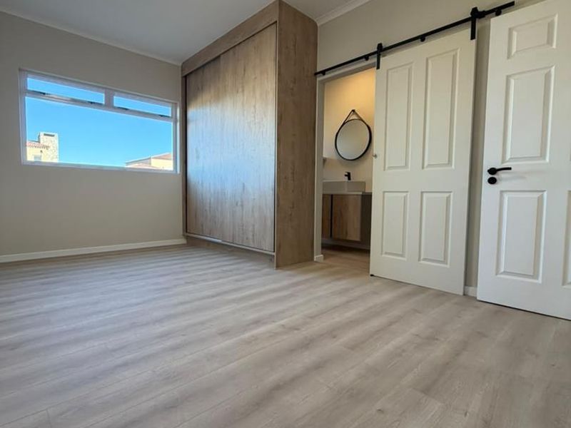 A bright, modern bedroom featuring light wood-look laminate flooring, a large built-in wardrobe, and a sliding barn door leading to an en-suite bathroom.