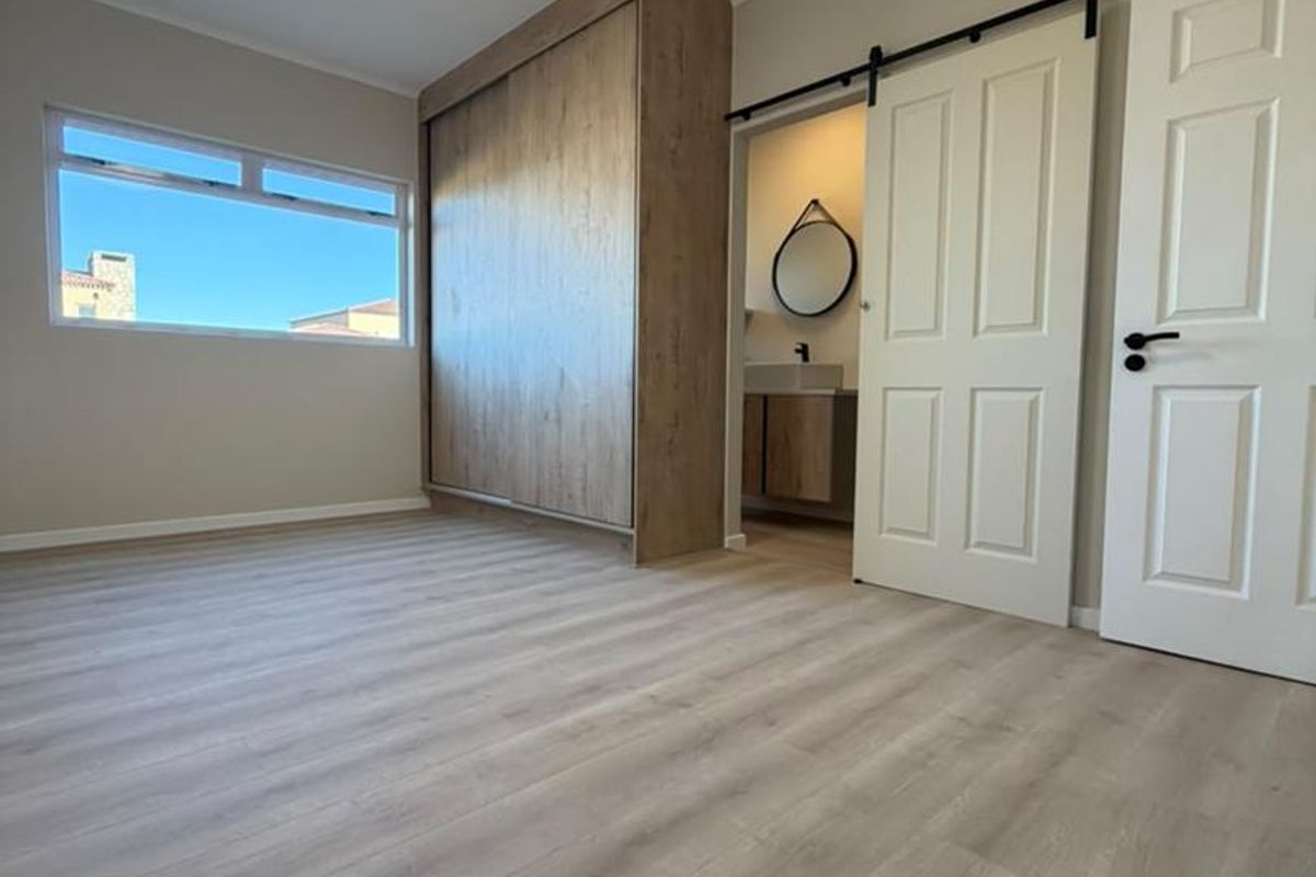 A bright, modern bedroom featuring light wood-look laminate flooring, a large built-in wardrobe, and a sliding barn door leading to an en-suite bathroom.