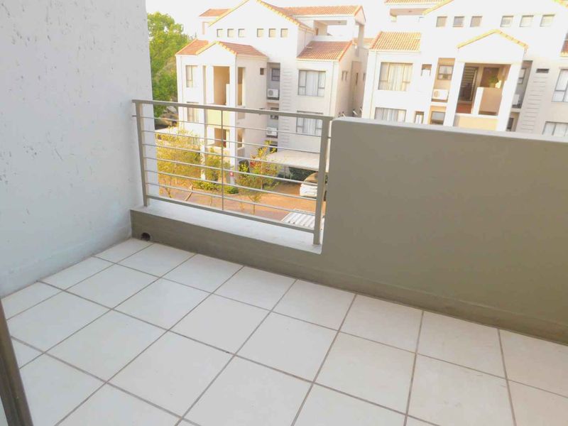 A clean, open-air balcony featuring tiled flooring and a secure metal balustrade, offering a view of the surrounding apartment complex.