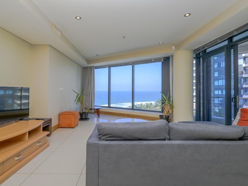 Spacious living room featuring large floor-to-ceiling windows with panoramic ocean views, tiled flooring, and recessed lighting.