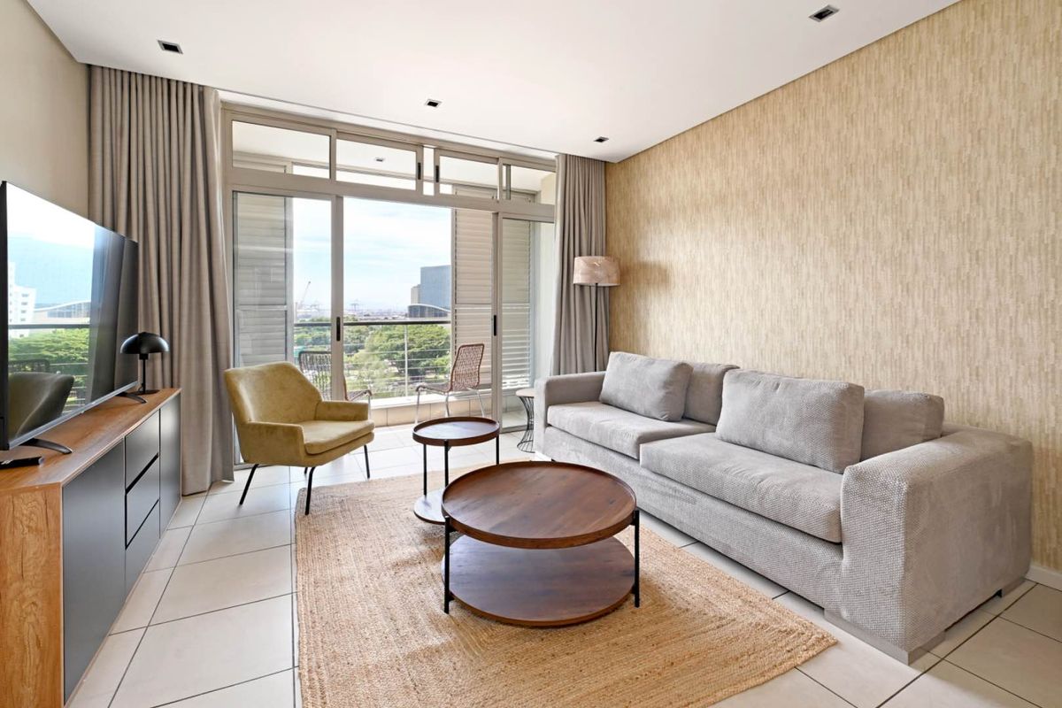 Modern living room featuring tiled floors, textured feature wall, and large sliding glass doors providing access to a balcony with city views.
