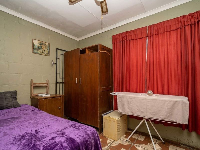 A bedroom featuring painted block walls, a ceiling fan, and tiled flooring, offering a functional space ready for cosmetic updates.