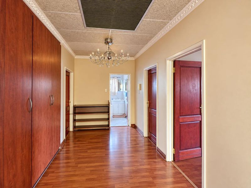 Spacious hallway featuring laminate flooring, extensive built-in storage cupboards, and classic ceiling detailing, providing access to multiple rooms.