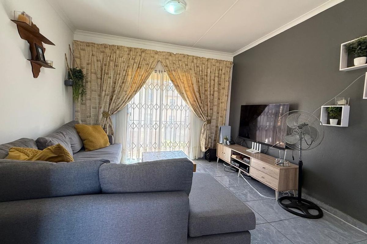 A comfortable living room featuring tiled flooring, a dark accent wall, and sliding glass doors with security gates leading to an outdoor area.