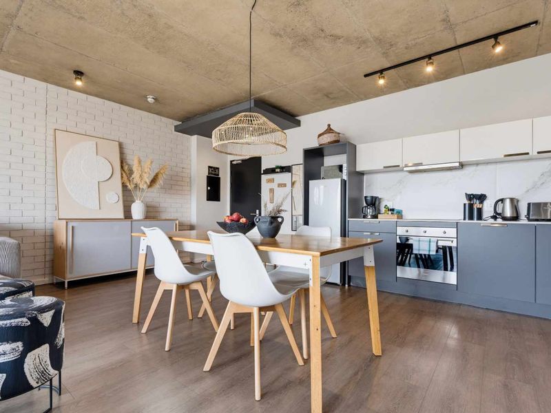 Modern open-plan living and kitchen area featuring an exposed concrete ceiling, white brick feature wall, and contemporary grey and white cabinetry.