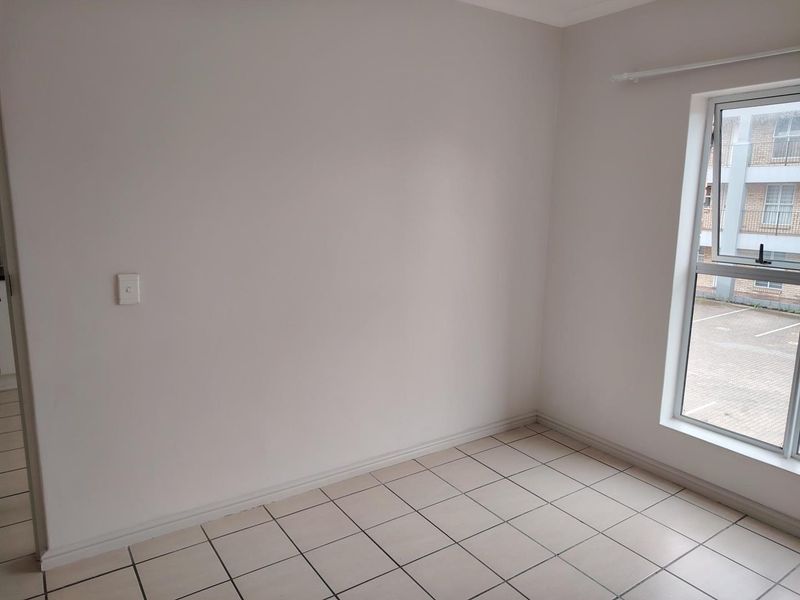An empty bedroom featuring neutral tiled flooring, a window with a curtain rail, and a clean, minimalist aesthetic ready for personalization.