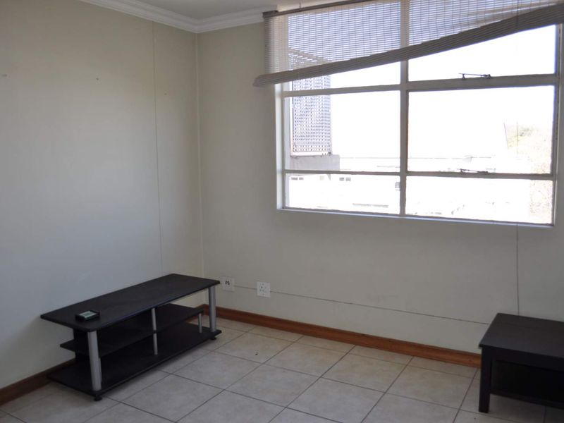 An empty living room featuring tiled flooring and a large window with a damaged blind, offering a blank canvas for potential interior updates.