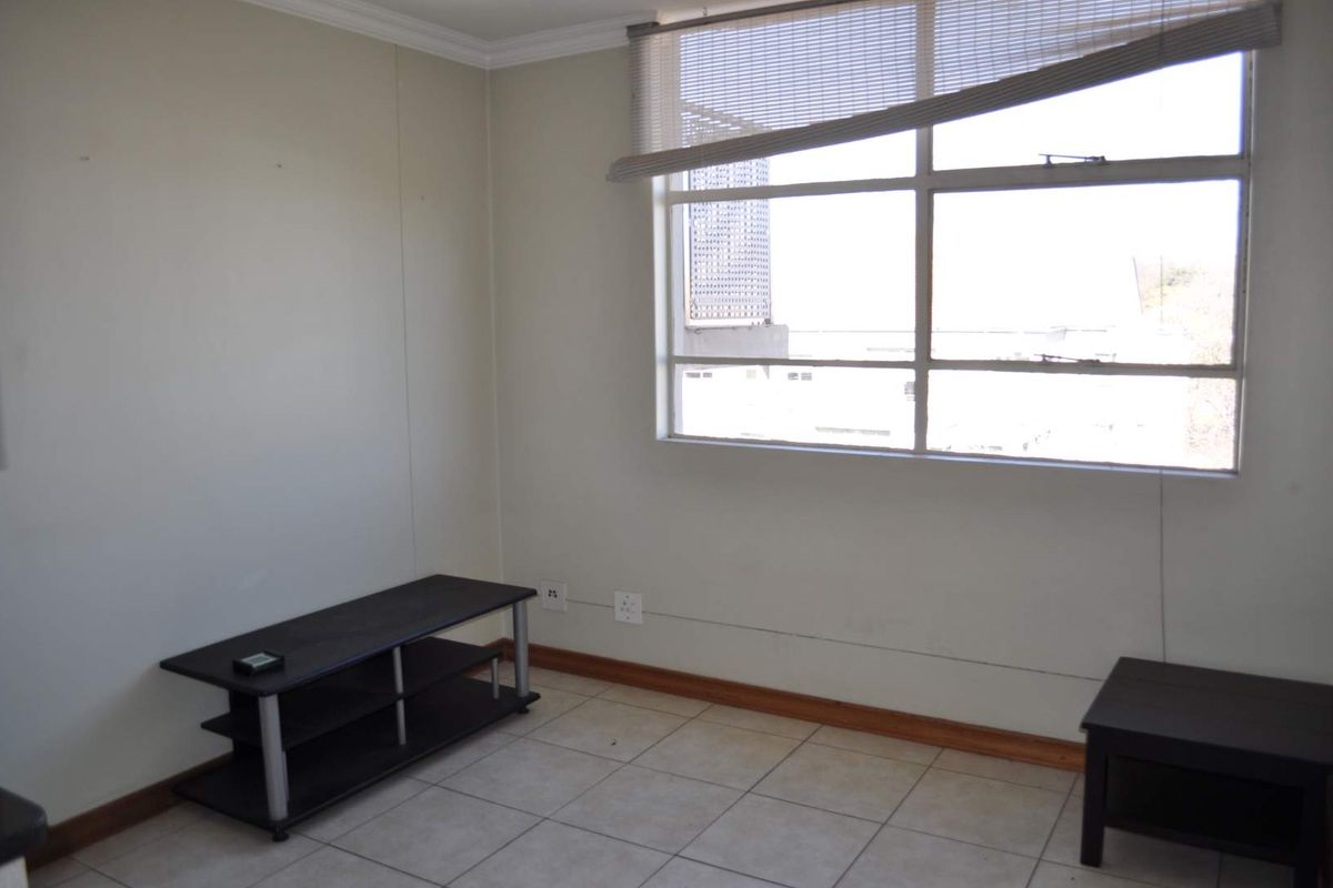 An empty living room featuring tiled flooring and a large window with a damaged blind, offering a blank canvas for potential interior updates.
