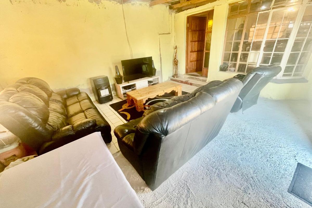 A living room area featuring exposed timber ceiling beams, unfinished wall surfaces, and a large multi-pane window, requiring cosmetic renovation to improve the finish.