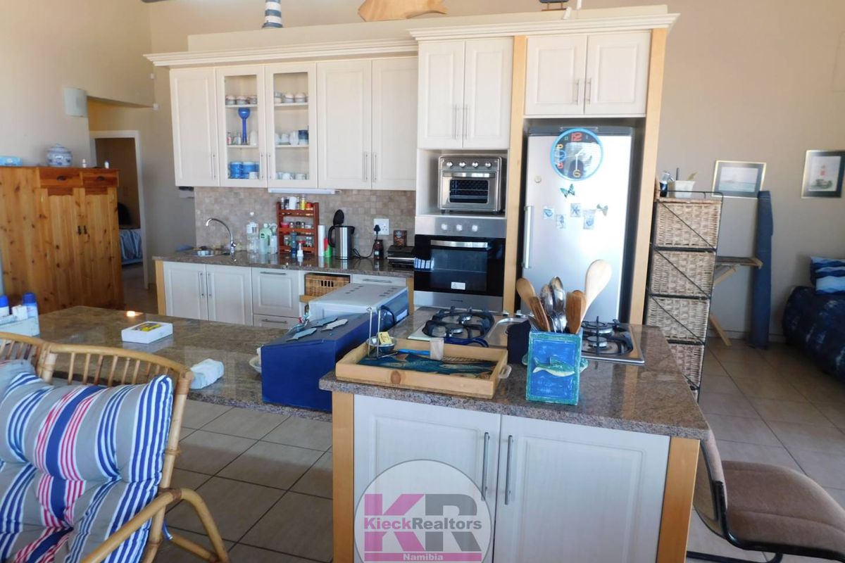A functional kitchen featuring granite countertops, built-in oven, gas hob, and cream-colored cabinetry with an integrated breakfast bar.