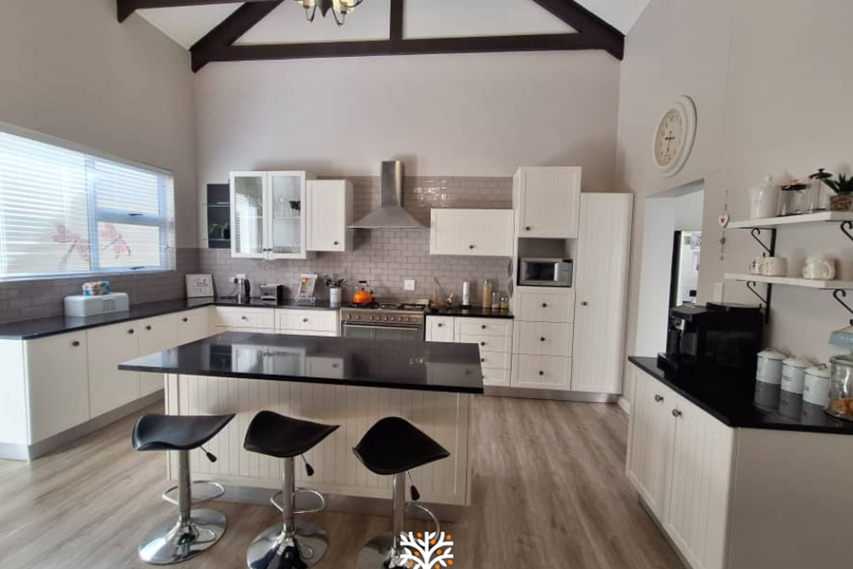 Spacious kitchen featuring white cabinetry, dark granite countertops, a central island with breakfast bar, and high vaulted ceilings with exposed timber beams.