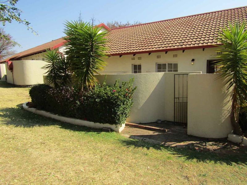 Rear view of the retirement unit featuring a tiled roof, stucco walls, and a private paved courtyard area with a security gate.