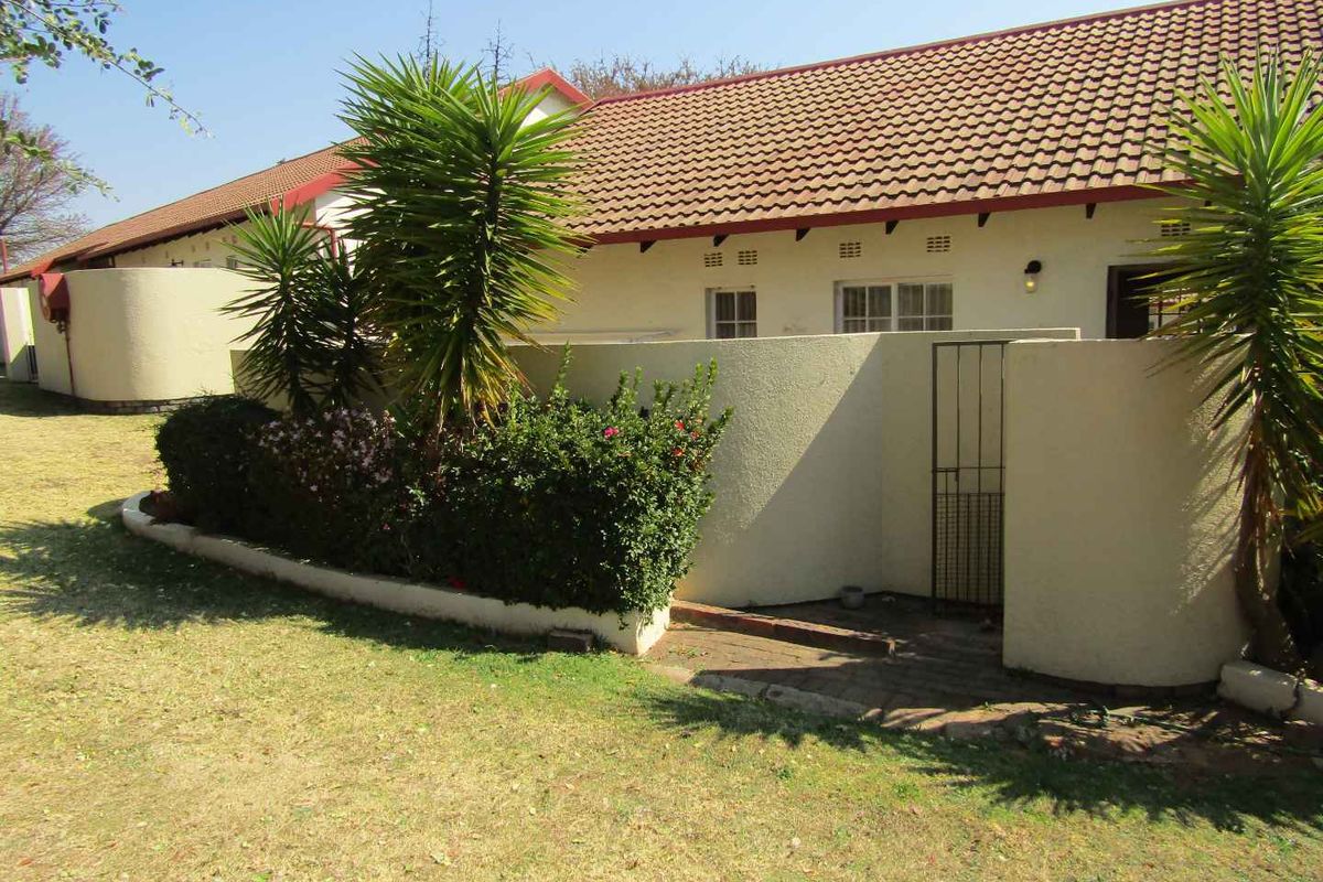 Rear view of the retirement unit featuring a tiled roof, stucco walls, and a private paved courtyard area with a security gate.