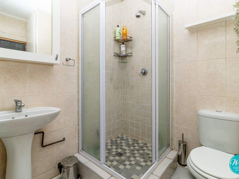 A functional bathroom featuring a pedestal basin, a corner shower enclosure, and a standard toilet with neutral wall tiling.