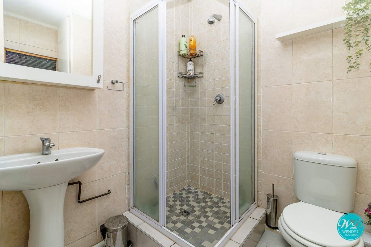 A functional bathroom featuring a pedestal basin, a corner shower enclosure, and a standard toilet with neutral wall tiling.