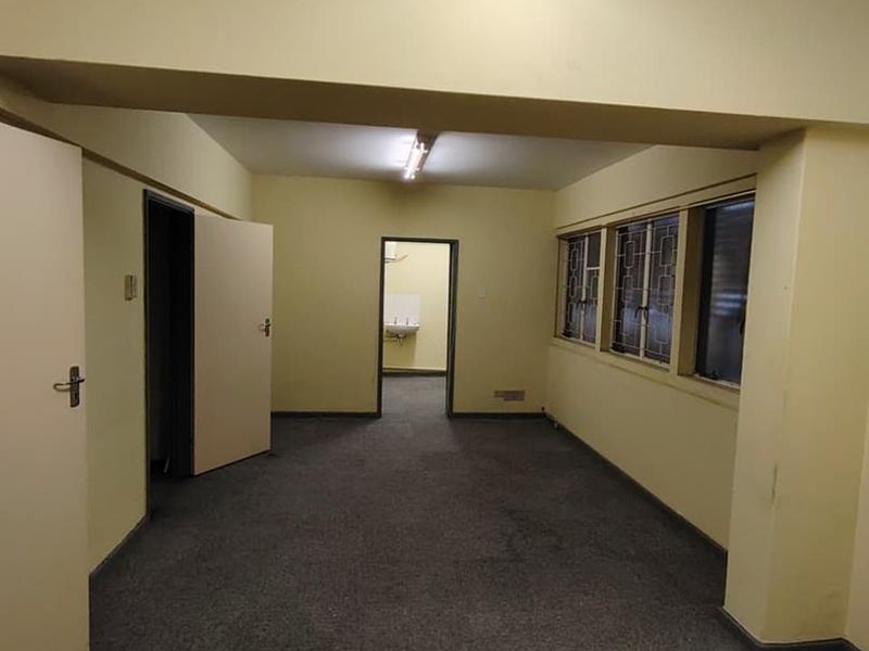 An empty, functional office space featuring carpeted flooring, fluorescent lighting, and security bars on the windows, offering a blank canvas for business use.