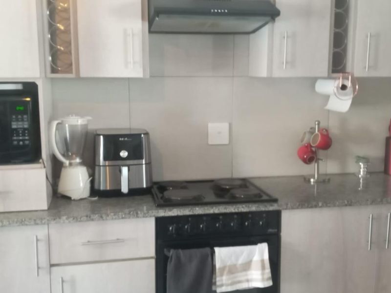 A functional kitchen featuring light-toned cabinetry, granite countertops, a built-in oven, electric hob, and an extractor fan with a tiled backsplash.