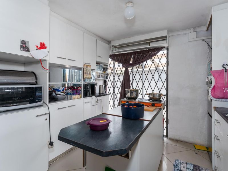 A compact kitchen featuring white built-in cabinetry, dark laminate countertops, and tiled flooring, with direct access to an exterior area via a security gate.