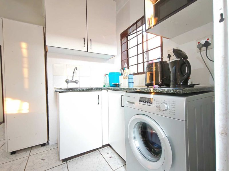 Compact scullery area featuring built-in white cabinetry, granite countertops, a stainless steel sink, and tiled flooring with security bars on the window.