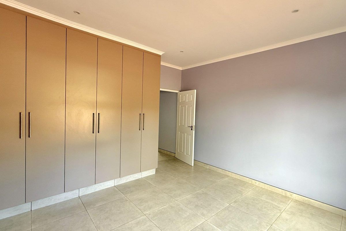 A clean, empty bedroom featuring neutral-toned built-in floor-to-ceiling wardrobes, tiled flooring, and recessed ceiling lighting.