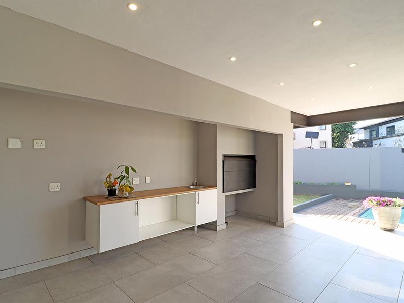 Covered patio area featuring a built-in braai, sink, and cabinetry, overlooking the pool and garden.