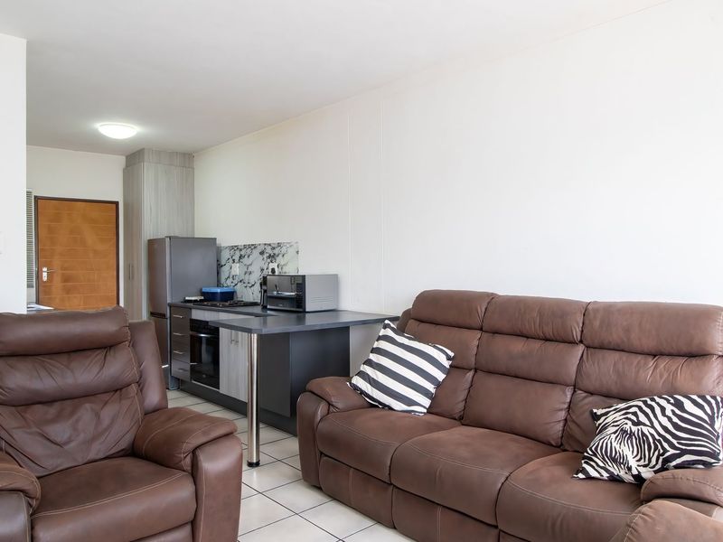 Open-plan living area featuring a compact kitchen with built-in cabinetry, oven, and hob, complemented by tiled flooring throughout the space.