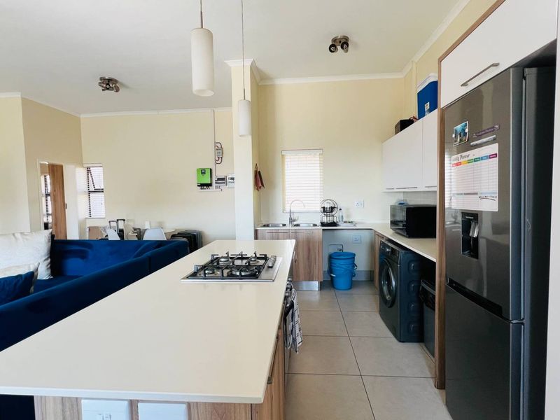 Open-plan living area featuring a modern kitchen with a central island, gas hob, tiled flooring, and ample built-in cabinetry.
