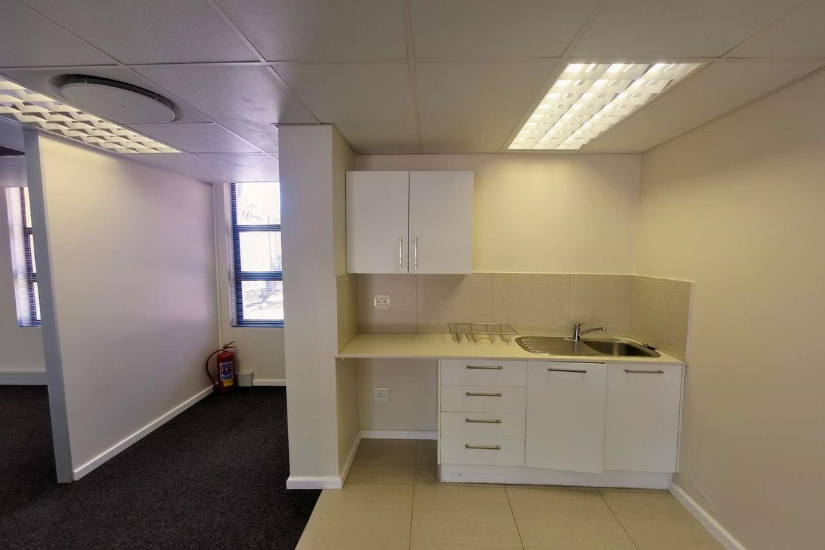 A functional office kitchenette featuring built-in cabinetry, a stainless steel sink, tiled splashback, and recessed ceiling lighting.