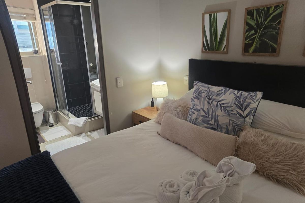 A well-maintained bedroom featuring an en-suite bathroom with a glass-enclosed shower and modern tiling.