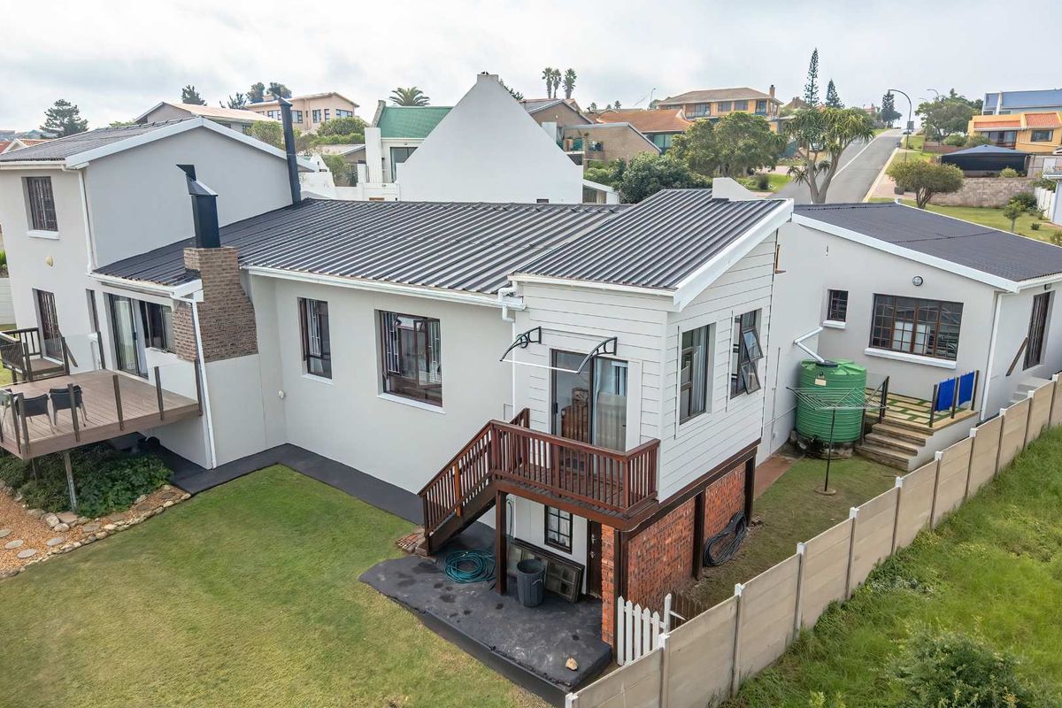 Aerial view of the rear property elevation featuring a raised wooden deck, metal roofing, and a landscaped garden area with a water tank.