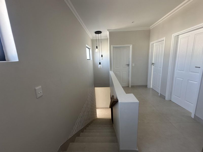 A bright and modern upper-level hallway featuring tiled flooring, clean neutral walls, and a staircase with a contemporary pendant light fixture.