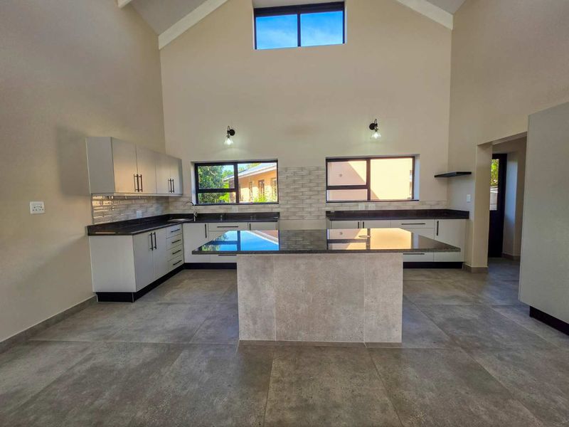 Modern, spacious kitchen featuring a central island, granite countertops, tiled backsplash, and high vaulted ceilings with a clerestory window for natural light.