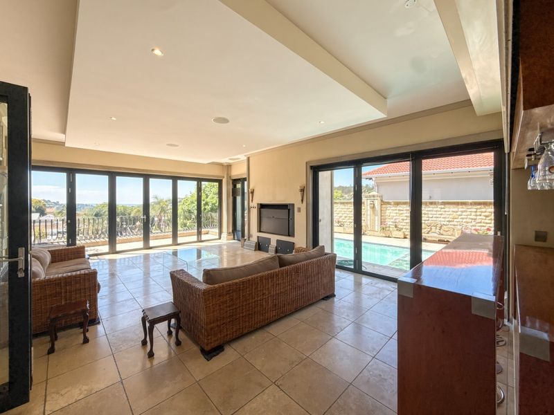 Spacious open-plan living area featuring large stacking glass doors, tiled flooring, a built-in fireplace, and a custom bar counter, opening onto the pool area.