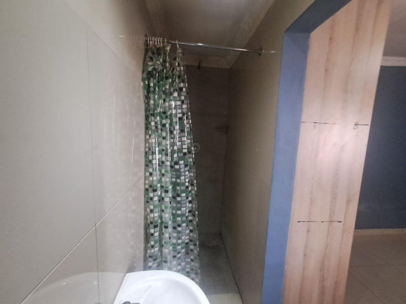 A small bathroom featuring a shower with a curtain and a pedestal basin, currently showing signs of unfinished wall and door frame work.