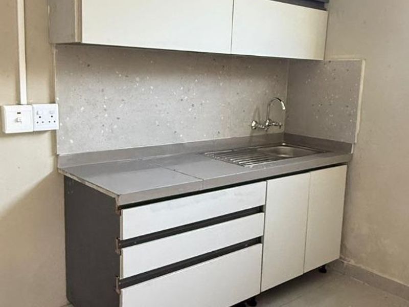 A compact kitchen area featuring modern two-tone cabinetry, a stainless steel sink, and tiled splashback, presenting a functional space ready for minor cosmetic updates.