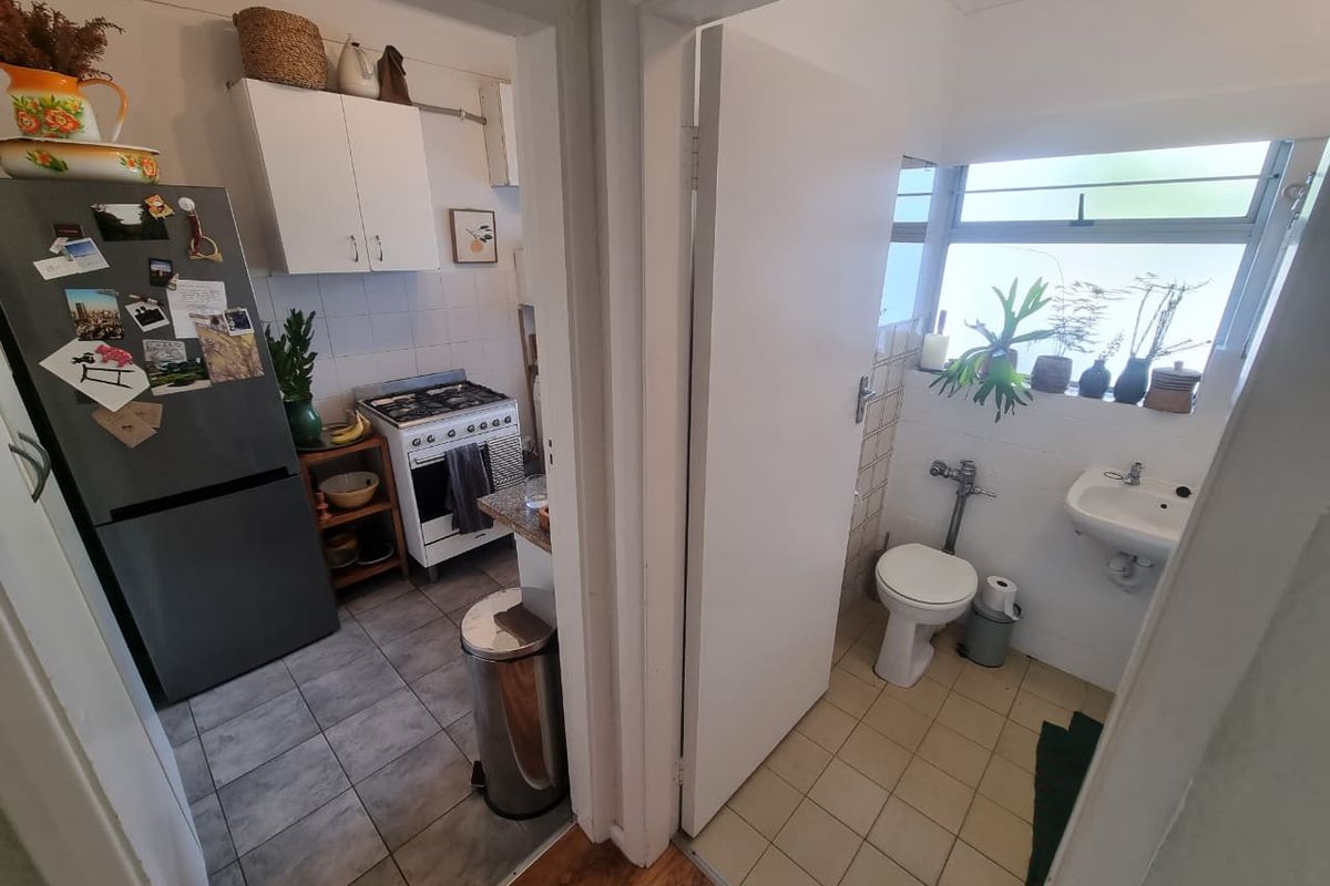 A view showing a compact kitchen with gas stove and cabinetry adjacent to a small bathroom with a toilet and basin.