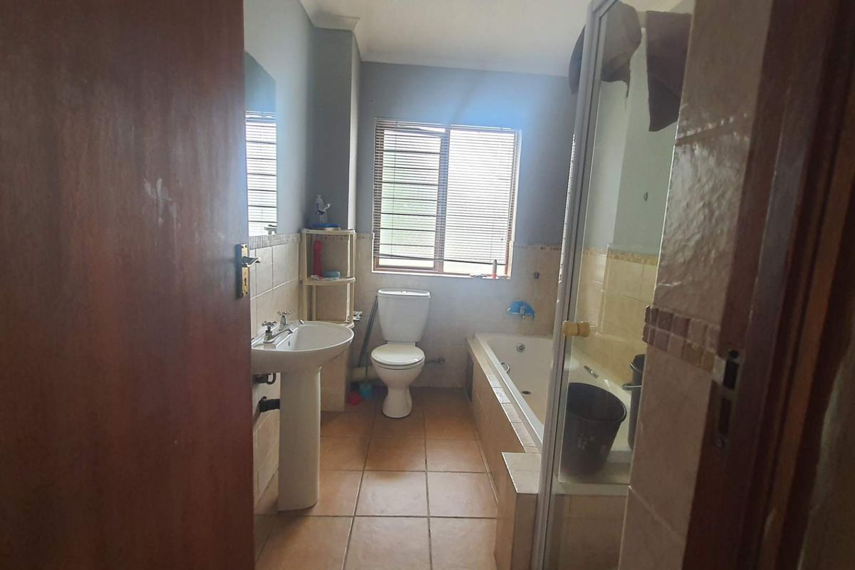 A functional bathroom featuring a pedestal sink, a built-in bathtub with shower enclosure, and a standard toilet, finished with ceramic floor tiles.