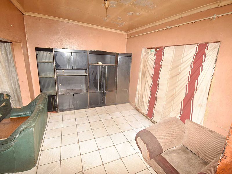 A living room space featuring ceramic floor tiles and a coved ceiling, currently requiring significant cosmetic renovation and repair to wall and ceiling finishes.
