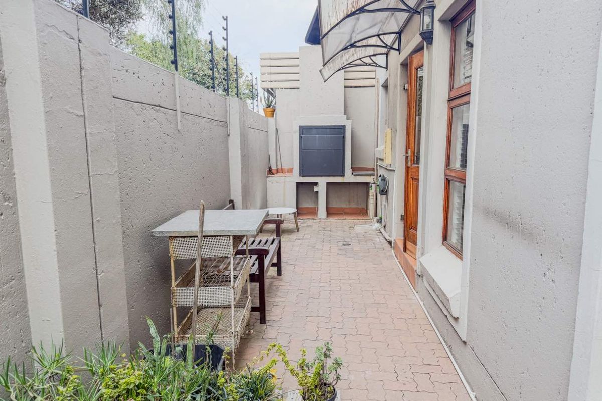 A private rear patio area featuring a built-in braai, paved flooring, and secure perimeter walling with electric fencing.