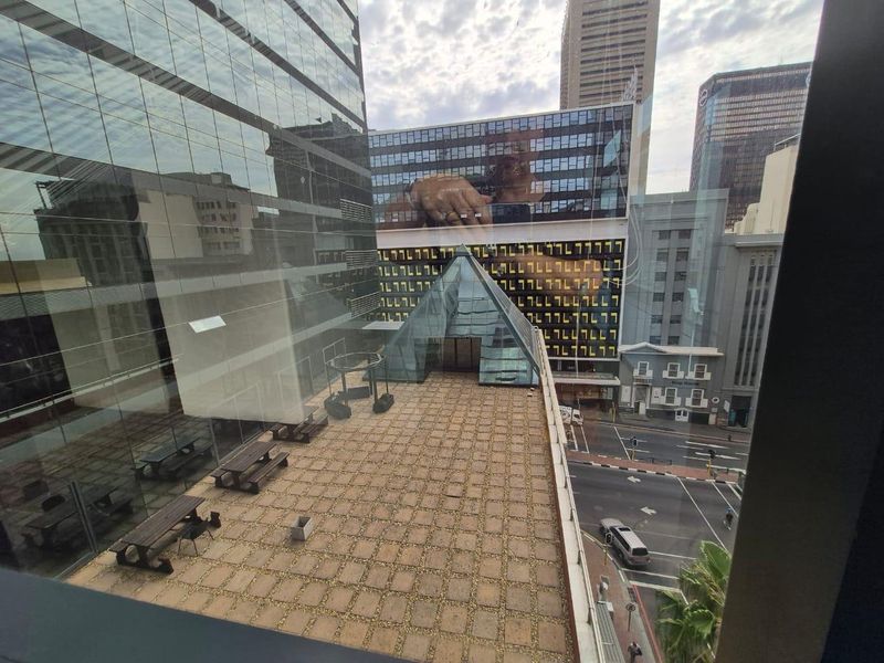 An elevated outdoor terrace featuring a glass pyramid skylight, overlooking a city street with surrounding high-rise office buildings.