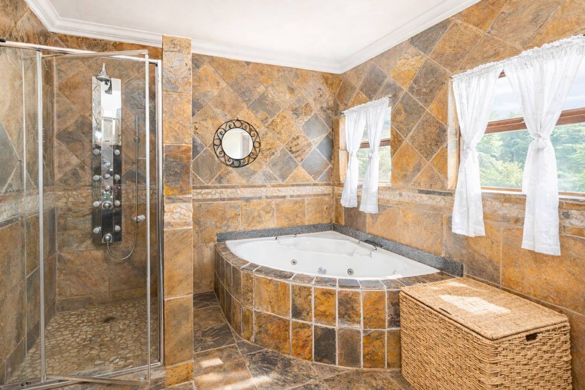 A bathroom featuring a corner jetted bathtub and a separate glass-enclosed shower with a multi-jet shower panel, finished with natural stone-style wall and floor tiles.