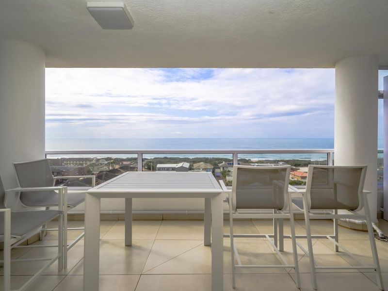 A spacious covered balcony featuring tiled flooring, a glass balustrade, and expansive ocean views.