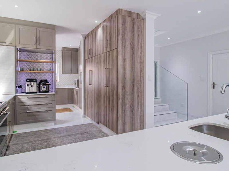 Modern kitchen featuring high-end cabinetry, quartz countertops, integrated appliances, a stylish scalloped backsplash, and a seamless transition to the staircase area.