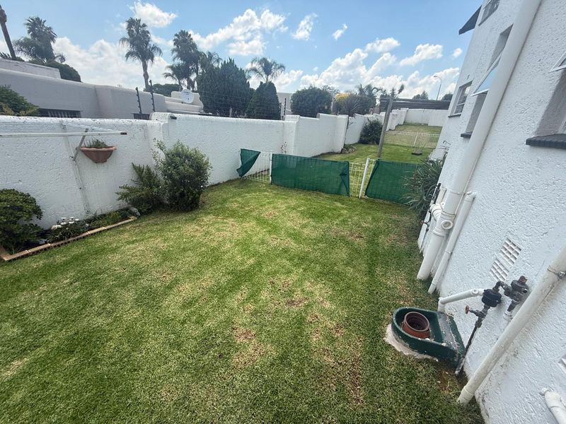 A private rear garden area featuring a lawn, boundary walls, and external utility plumbing, offering potential for landscaping and outdoor improvement.