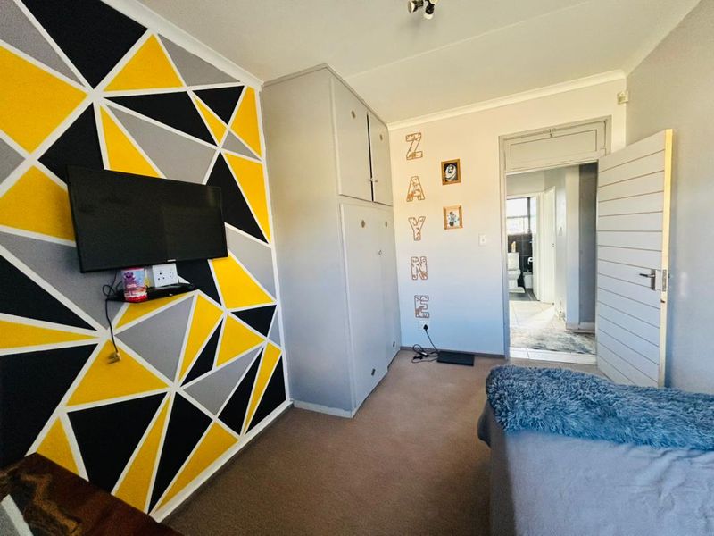 A bedroom featuring built-in cupboards, carpeted flooring, and a geometric accent wall, with an adjoining view into a bathroom.
