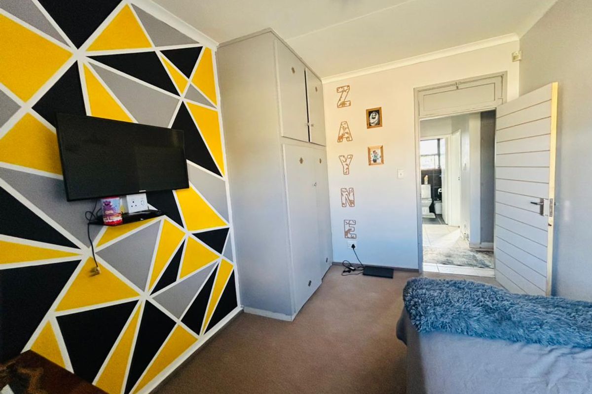 A bedroom featuring built-in cupboards, carpeted flooring, and a geometric accent wall, with an adjoining view into a bathroom.